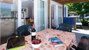 Un área de comedor al aire libre con una mesa dispuesta para dos, una computadora portátil, un bol de cerezas, una botella de vino y un libro.