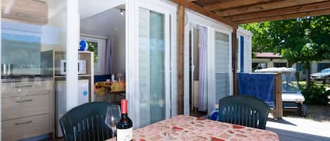 Un área de comedor al aire libre con una mesa dispuesta para dos, una computadora portátil, un bol de cerezas, una botella de vino y un libro.