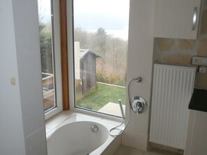A bathroom with a bathtub, a shower, and a view of a garden and a building outside. - Luxurious Apartment in Waldeck With Sauna (Waldeck)
