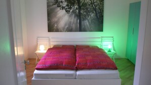 A bedroom with a bed, two bedside lamps, a green wall, and a painting of trees. - Luxurious Apartment in Waldeck With Sauna (Waldeck)