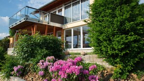 A modern two-story house with large windows, a balcony, and a well-maintained garden with flowering plants. - Luxurious Apartment in Waldeck With Sauna (Waldeck)