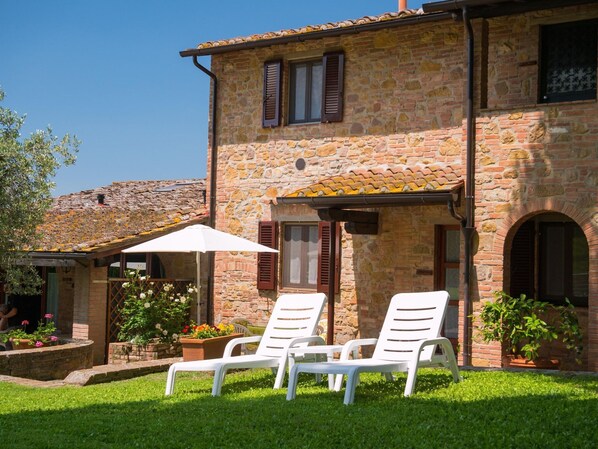 A stone building with a tiled roof, two white lounge chairs, and potted plants. - Charming Retreat in Montaione (Montaione)