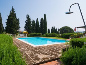 A rectangular swimming pool with a tiled deck, surrounded by greenery and trees. - Charming Retreat in Montaione (Montaione)