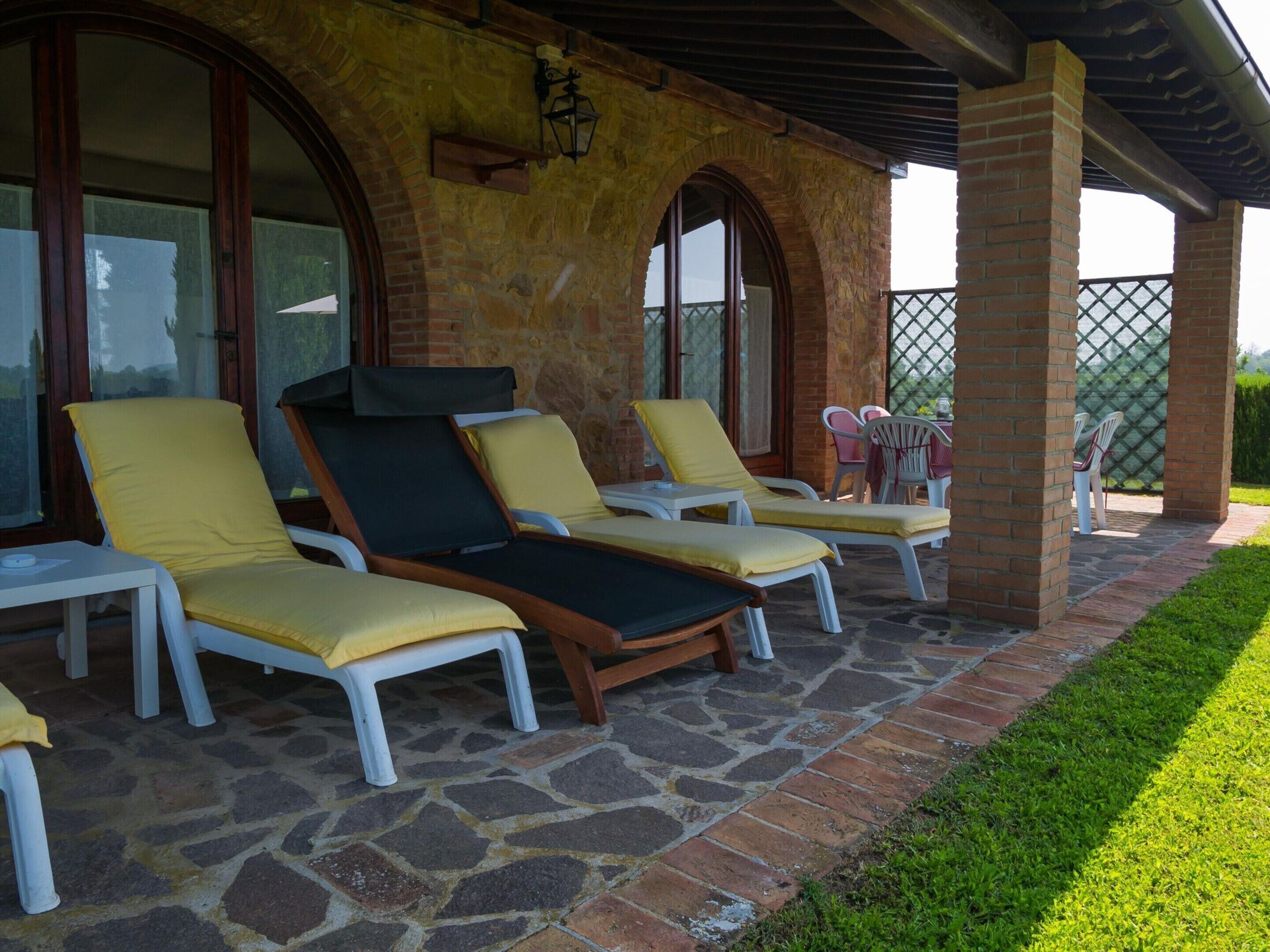 Een overdekt terras met stenen vloer en bakstenen muren, voorzien van meerdere lounge fauteuils.