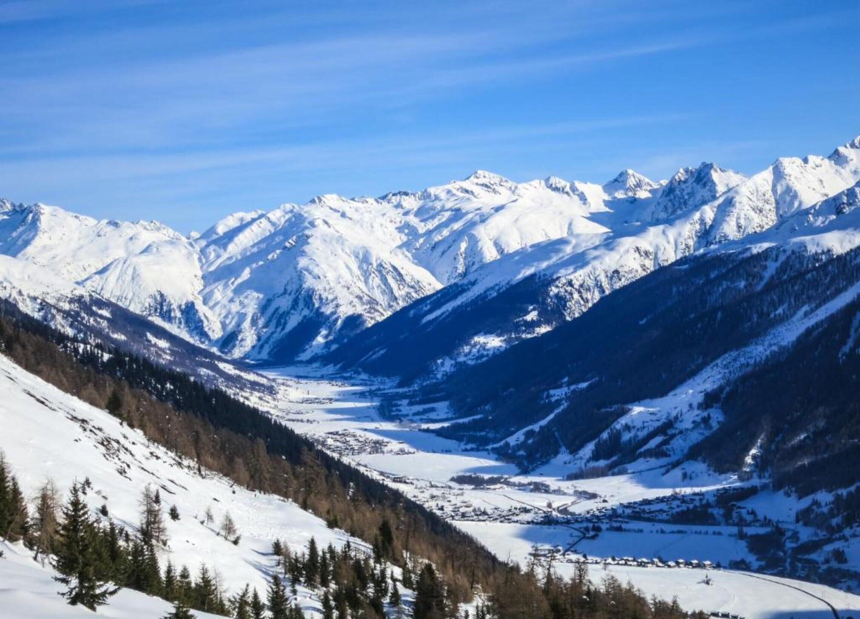 Paisagem montanhosa coberta de neve, com um vale e um pequeno povoado.