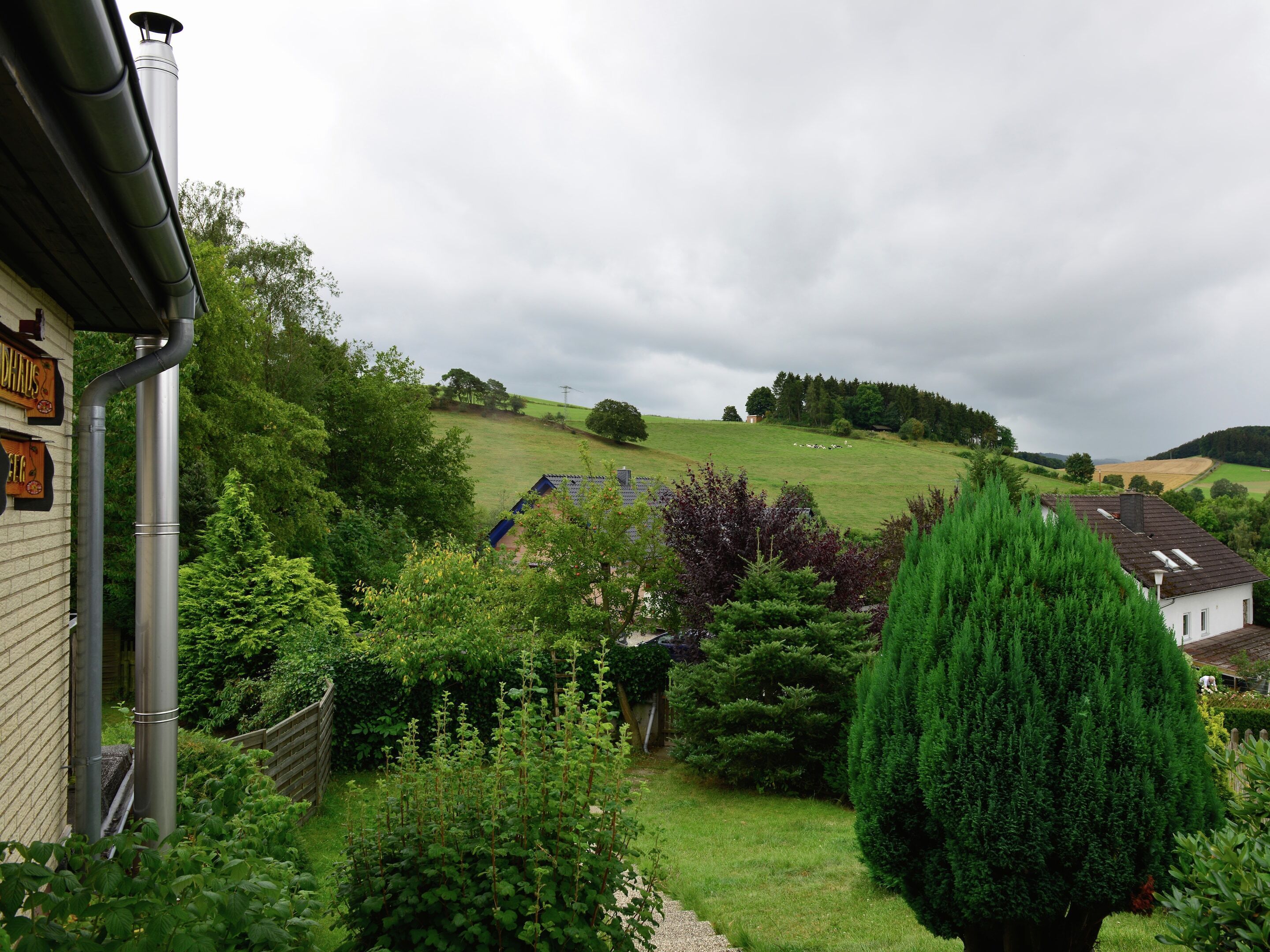A rural landscape with a house, a garden, and a hill in the background.