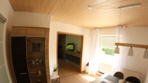 Ein Essbereich mit Tisch und Stühlen, eine Küche mit Kühlschrank und Schränken sowie ein Wohnbereich mit Fernseher.