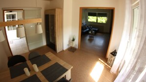 Ein modernes Wohnzimmer mit Holzbalkendecke, einem Essbereich mit Tisch und Stühlen und Blick auf einen Garten durch eine Tür.