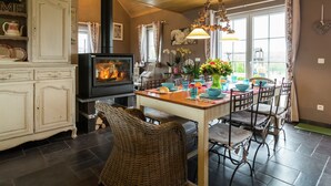 Una habitación acogedora con chimenea, una mesa de comedor, sillas de mimbre y vistas al exterior.