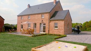 Una casa de ladrillo con techo inclinado, un patio con mobiliario exterior y un arenero al frente.