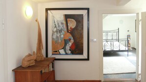 Un corridoio con un quadro astratto incorniciato, una scultura in legno e una ringhiera metallica che conduce a un'altra stanza.