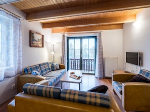 Ein gemütliches Wohnzimmer mit einer Sofagarnitur, einem Couchtisch und einem an der Wand befestigten Fernseher.