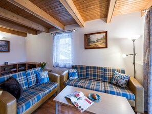 Ein gemütliches Wohnzimmer mit Karomöbeln, einer Holzbalkendecke, einem gerahmten Landschaftsbild und einem Tisch mit einer Zeitschrift und einem Croissant.