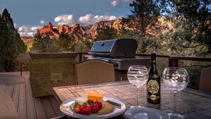 An outdoor dining area with a grill, a bottle of wine, and a plate of food. - Stunning Luxury Home, Amazing Views! Painted Cliff (Sedona)