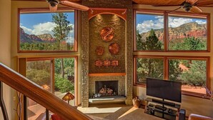 A spacious living room with a fireplace, large windows, and a television. - Stunning Luxury Home, Amazing Views! Painted Cliff (Sedona)
