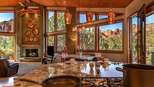 A kitchen with a large island, stone fireplace, and large windows with a mountain view. - Stunning Luxury Home, Amazing Views! Painted Cliff (Sedona)