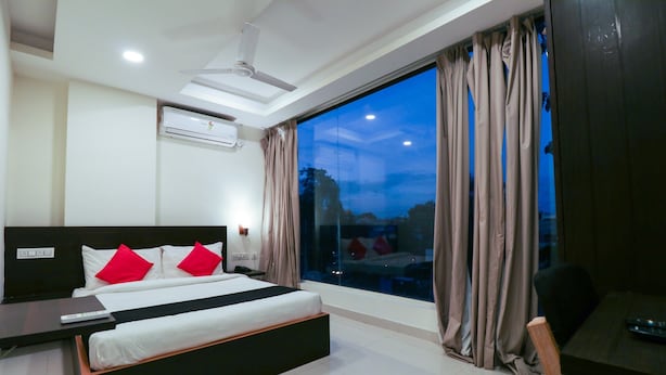 A modern hotel room with a large bed, a desk, and a view of the city at dusk. - Capital O 67657 Schmear Suites (Bengaluru)