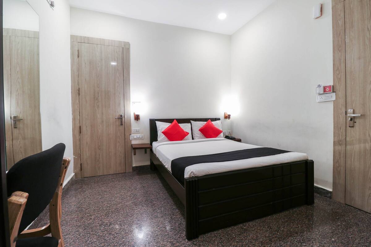 Hotellihuone, jossa on sänky, tuoli, yöpöytä ja puinen vaatekaappi.