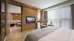 A hotel room with a bed, a TV mounted on the wall, a chair, a small table, and a window with curtains. - Shenzhen Hongdu Hotel (Shenzhen)