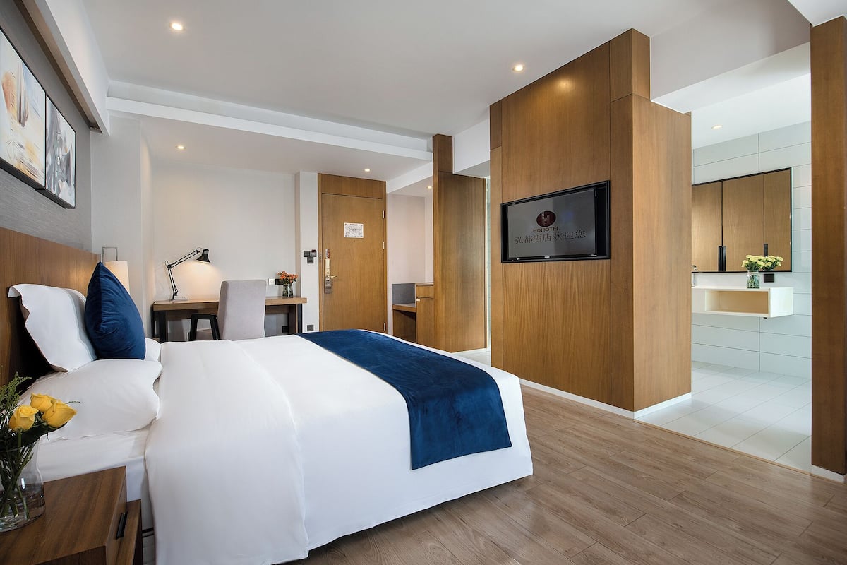 Ein modernes Hotelzimmer mit einem großen Bett, einem Schreibtisch und einem durch eine offene Tür einsehbaren Badezimmer.