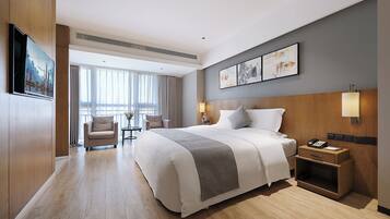 Habitación de hotel moderna con una cama grande, un escritorio, una silla y vistas de la ciudad a través de amplios ventanales.