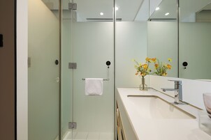 A modern bathroom with a glass shower enclosure, a white sink, and a mirror reflecting a vase of flowers.