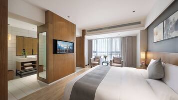 A modern hotel room with a large bed, a TV, a desk, and a view of the cityscape through the window.