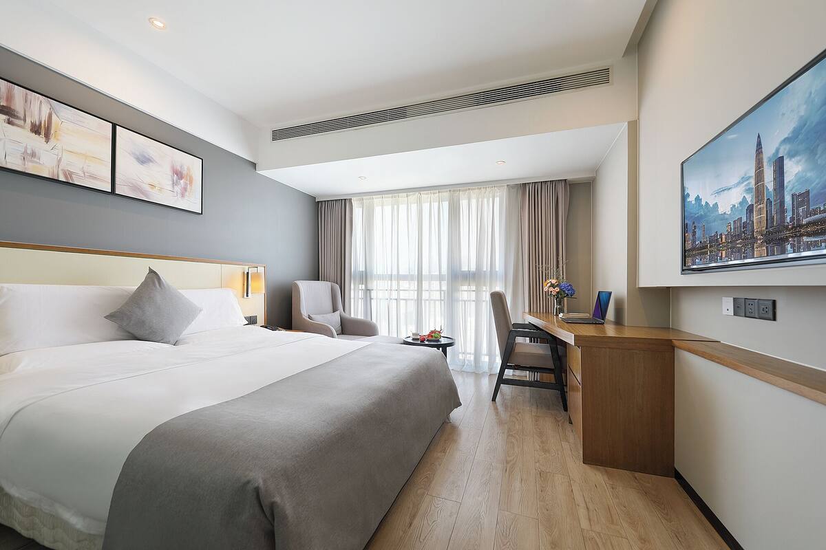 Ein Hotelzimmer mit einem großen Bett, einem Schreibtisch, einem Sessel und einem Stadtbild an der Wand.