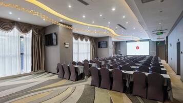 A conference room with rows of tables and chairs, a large screen, and a projector.