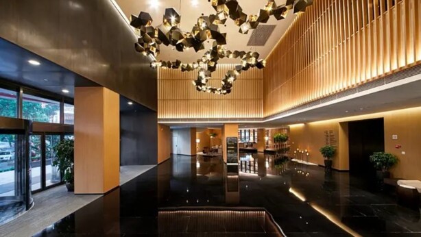 A modern hotel lobby with a reflective black floor, a central seating area, and a unique geometric light fixture.