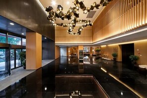 Un moderno vestíbulo de hotel con piso negro reflectante, un área de estar central y una lámpara geométrica única.