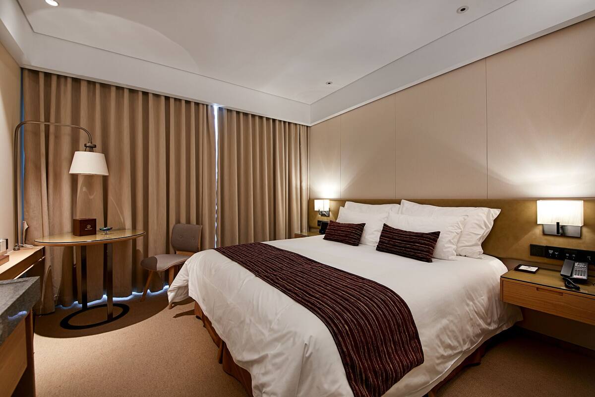 A modern hotel room with a large bed, bedside tables, a desk, and a chair.