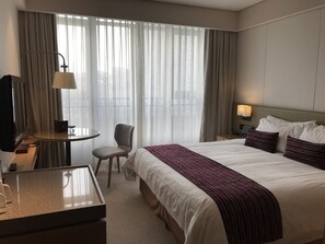 A hotel room with a bed, a desk, a chair, a lamp, and a window with curtains.