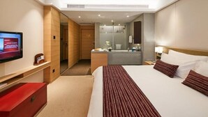 A hotel room with a large bed, a TV on the left, a bathroom with a mirror, and a red storage unit.