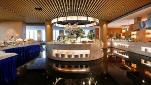 A modern hotel lobby with a central circular bar area, a long reception desk, and a polished floor reflecting the ceiling lights.
