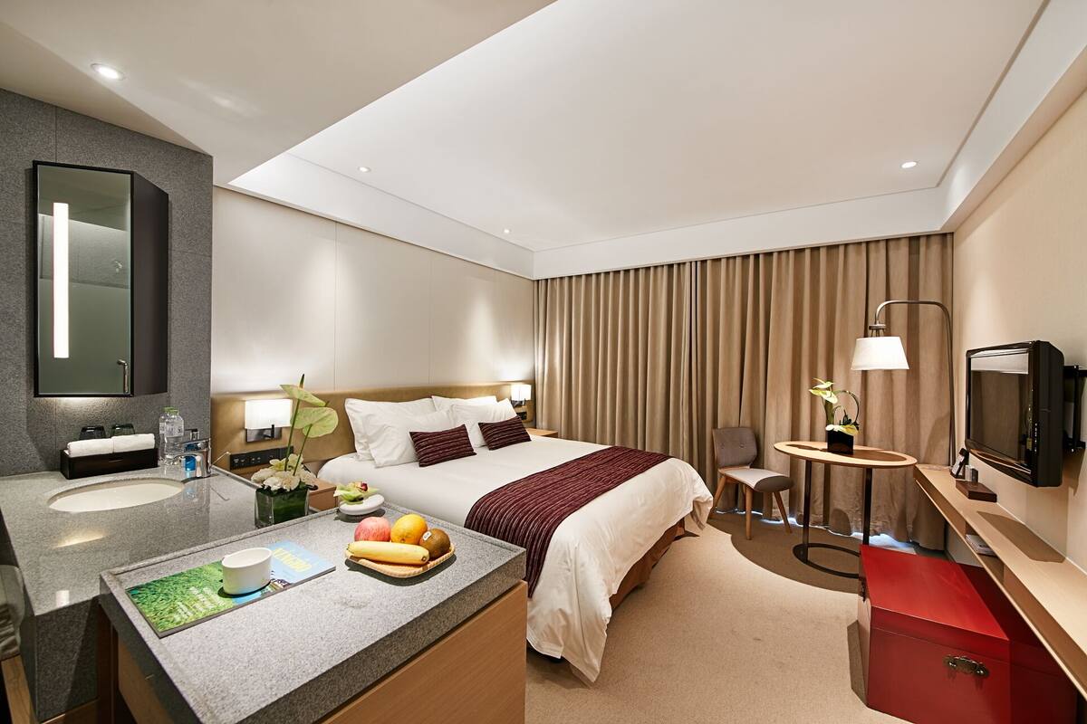 A modern hotel room with a large bed, a desk, a vanity with a mirror, and a television.