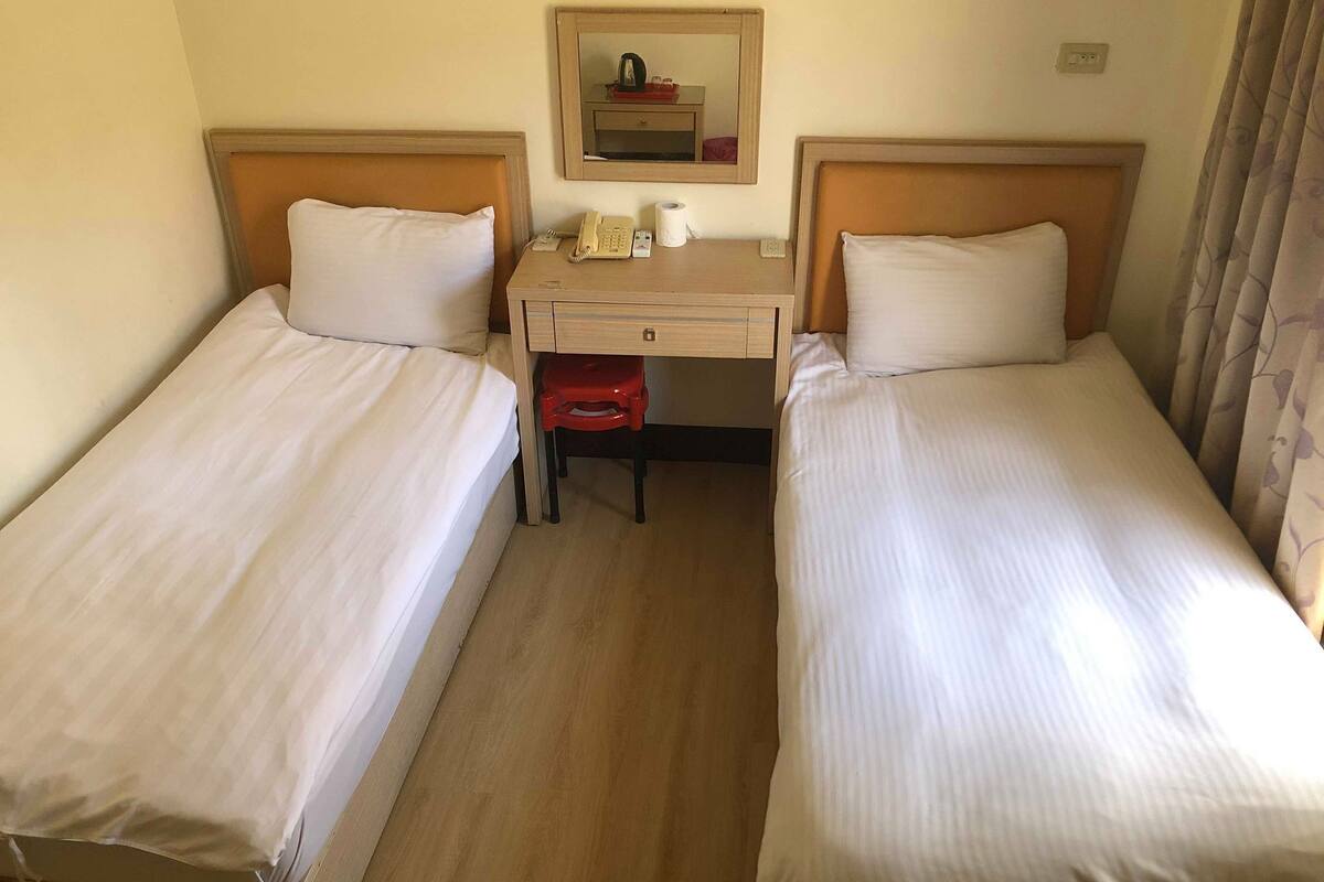 Habitación de hotel con dos camas individuales, un escritorio con teléfono y una taza, y un espejo sobre el escritorio.