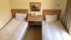 A hotel room with two single beds, a desk with a telephone and a cup, and a mirror on the wall. - Huasin Hotel (Jincheng)