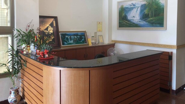 A reception area with a wooden counter, a painting of a waterfall, and three clocks on the wall. - Huasin Hotel (Jincheng)