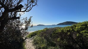 A coastal path leading to a beach with clear skies and distant islands.