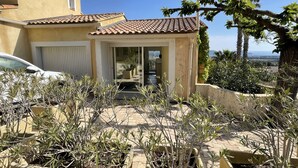 A Mediterranean-style house with a tiled roof, a sliding glass door entrance, and a garden with various plants. - DUPLEX APARTMENT, SEA VIEW (La Cadière-d'Azur)