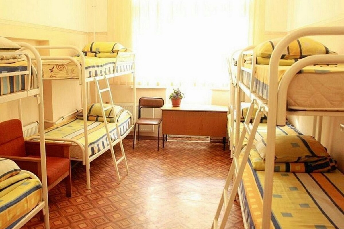 A dormitory room with bunk beds, a desk, and a chair.