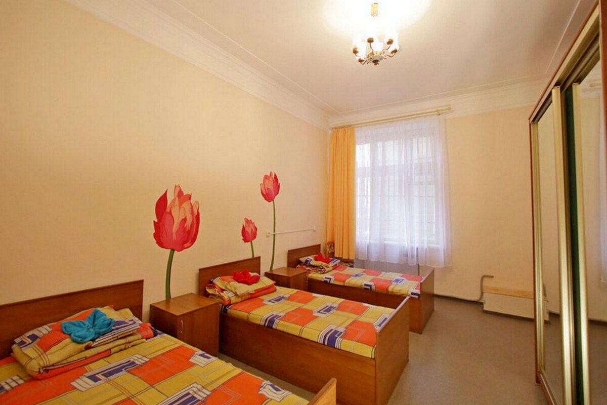 A hotel room with two single beds, a large mirror, a window with curtains, and a chandelier.