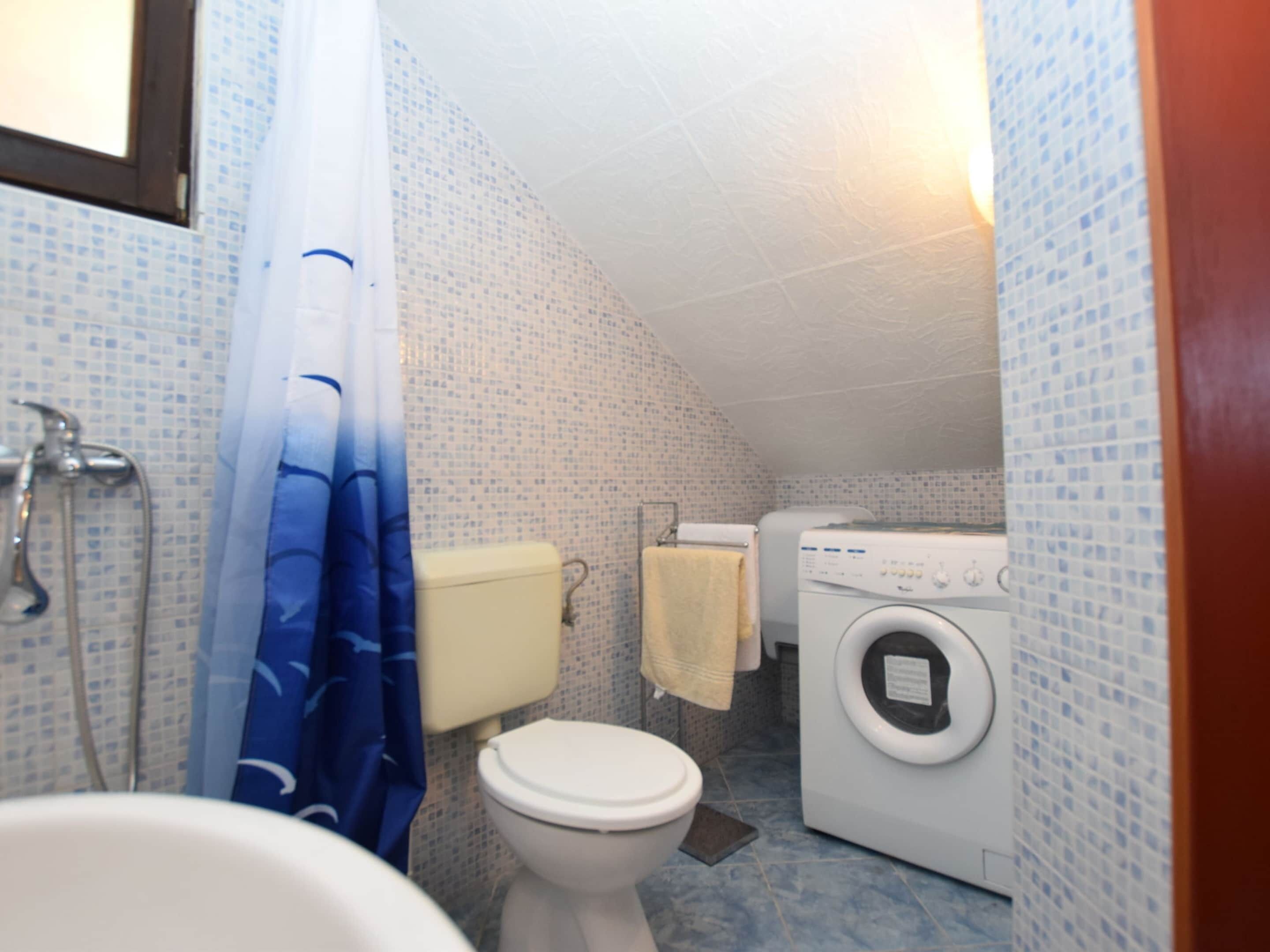 Casa de banho pequena com mosaicos, com sanita, máquina de lavar roupa e chuveiro.