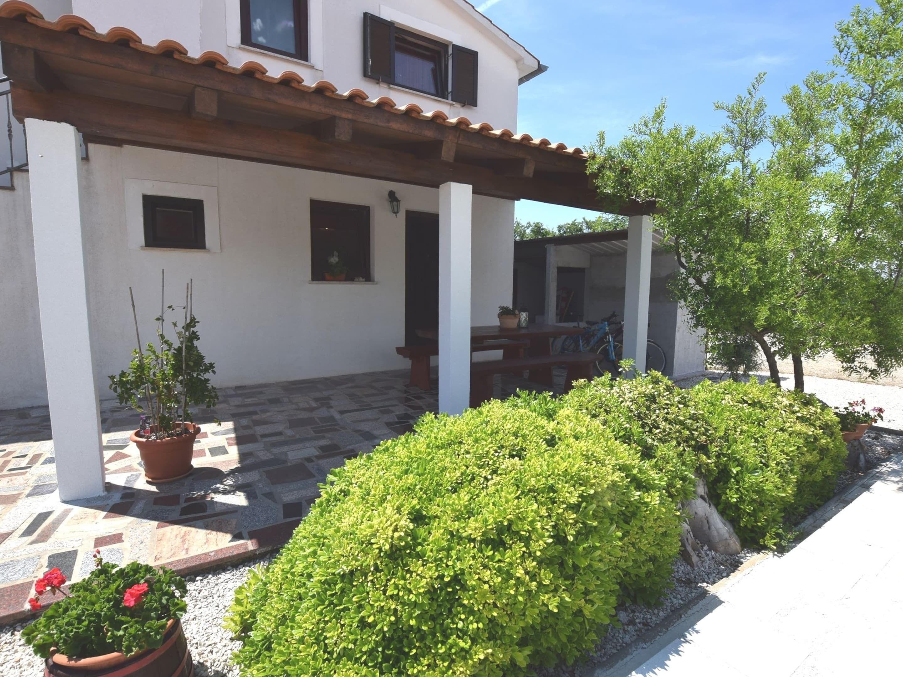 A white building with a tiled patio, potted plants, and a pergola.