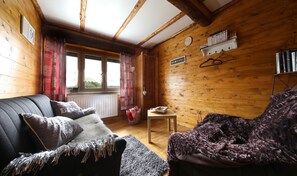 Une pièce chaleureuse avec des murs en bois, un canapé, un fauteuil, une petite table et une bibliothèque.