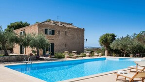 A pool area with lounge chairs, a stone building, and a view of the sea. - Villa in Paceco Near Marsala Beaches (Paceco)