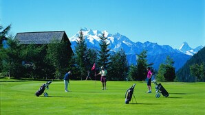 Un campo de golf con montañas al fondo, una cabaña de madera y varios golfistas.