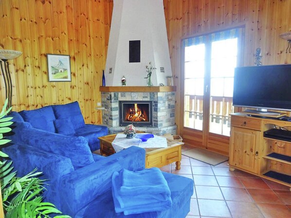 A cozy living room with a stone fireplace, a blue sofa, a television, and wooden walls.
