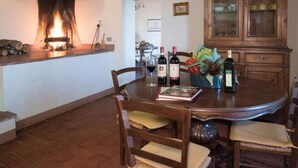 A dining area with a fireplace, wooden chairs, a table with wine bottles, and a cabinet with dishes. - Apartment in Tuscany With Stunning Hilltop Views (Pergine Valdarno)